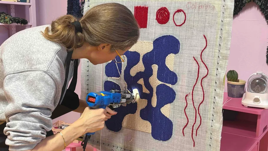 Person using tufting gun on textile design.