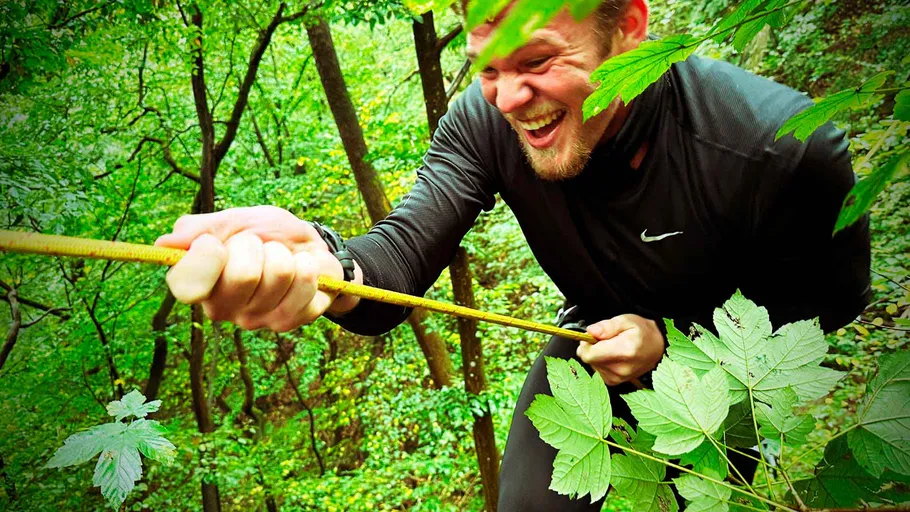 Man climbing rope in a lush forest.