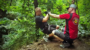 Two men preparing for zipline in forest.