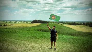 Person hält Fahne in ländlicher Landschaft.