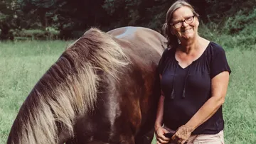 Woman smiling beside a grazing horse in field.