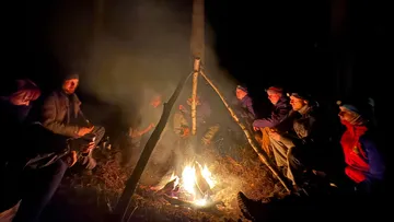 Menschen sitzen nachts um ein Lagerfeuer.