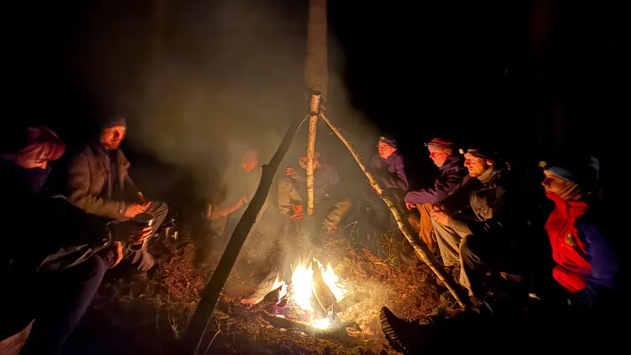 Menschen sitzen nachts um ein Lagerfeuer.