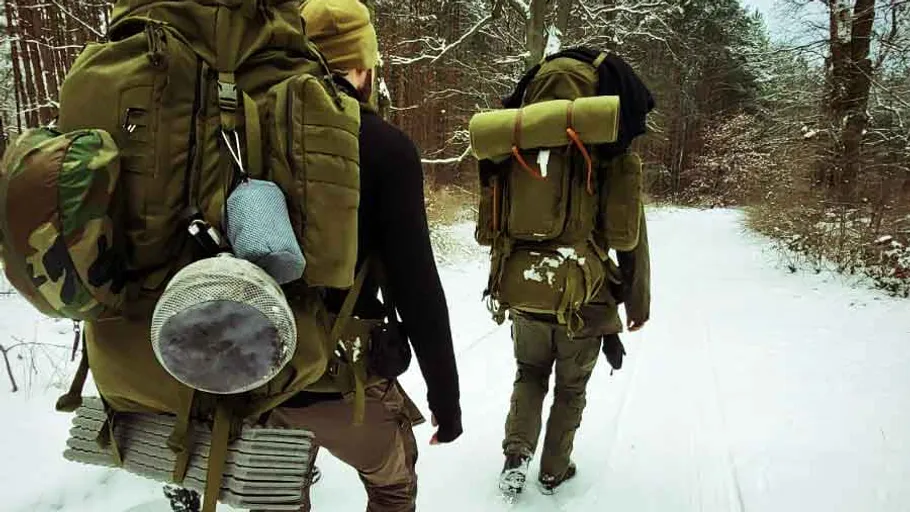 Two backpackers walking in snowy forest.