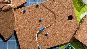 Korkplatte mit Schnur und blauen Perlen.