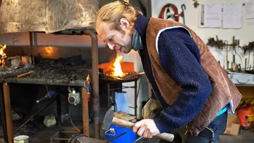 Blacksmith hammering metal in forge workshop.