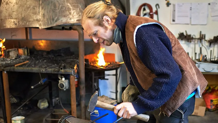 Schmied hämmert Metall in Schmiedewerkstatt.