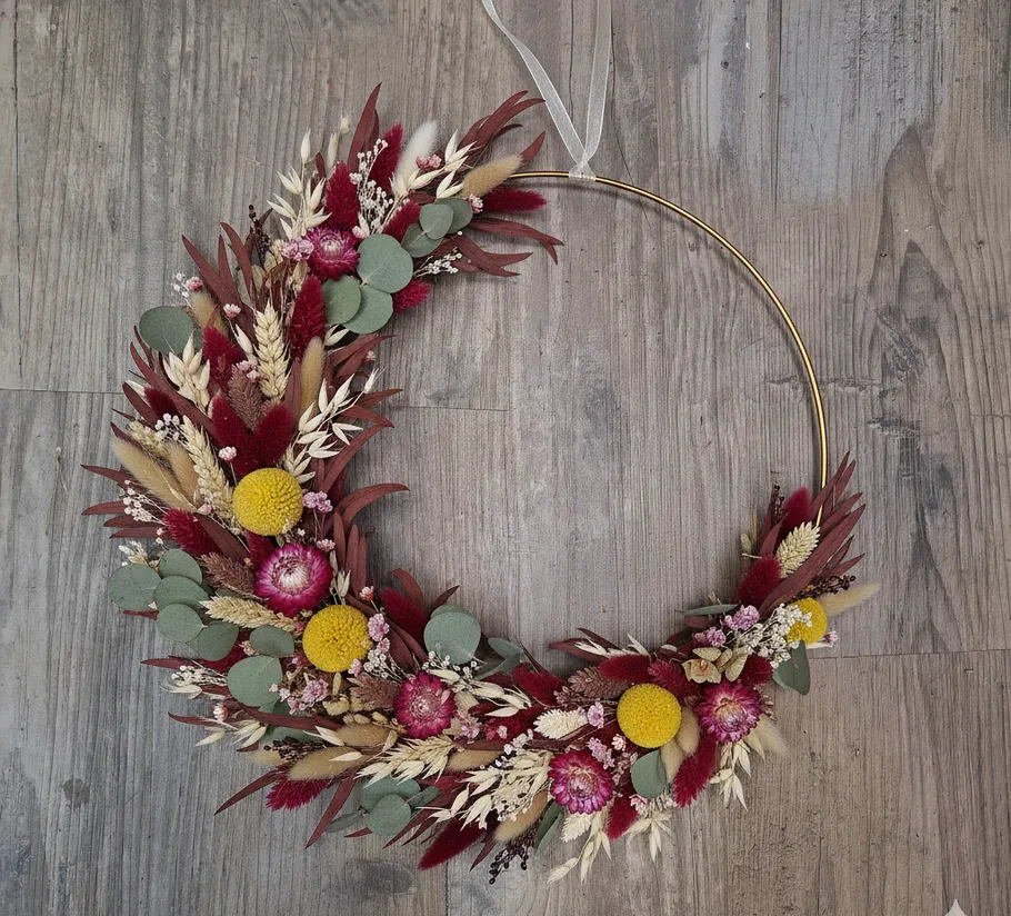 Blumenkranz mit gelben und roten Blumen auf Holz.