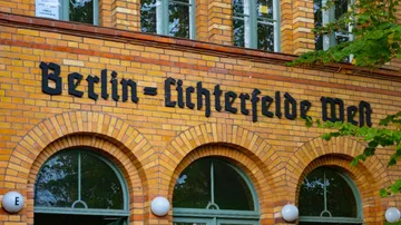 Gelbes Backsteingebäude mit Stationsname, Bäume.