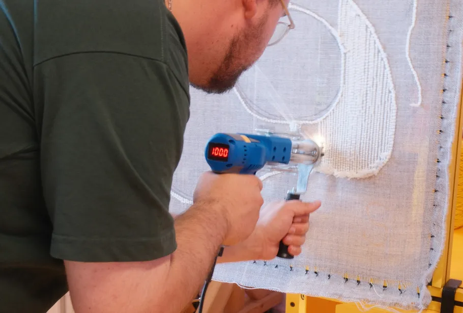 Person uses a tufting gun on canvas.