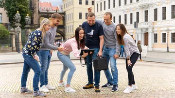 Gruppe im Freien schaut lachend auf ein Tablet.