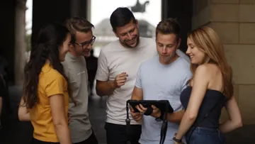 Fünf Personen schauen auf Tablet drinnen.