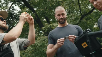 Three men examining a camera outdoors.