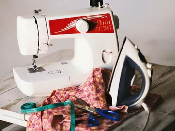 Sewing machine sews fabric on a table with accessories.