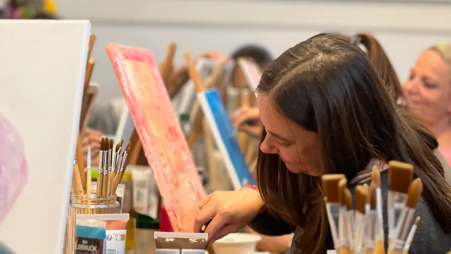 Woman painting in art class, surrounded by brushes.