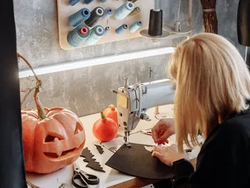 Sewing machine sews black fabrics on a table with pumpkins.