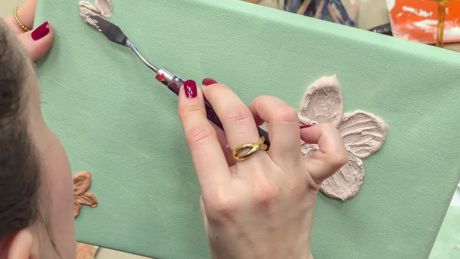 Person verwendet Spachtel auf Blumenleinwand.