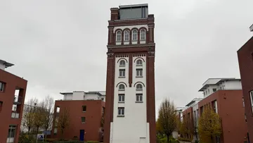 Hohes Ziegelgebäude umgeben von Wohngebäuden.