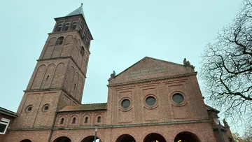Brick church with tall tower, overcast sky.