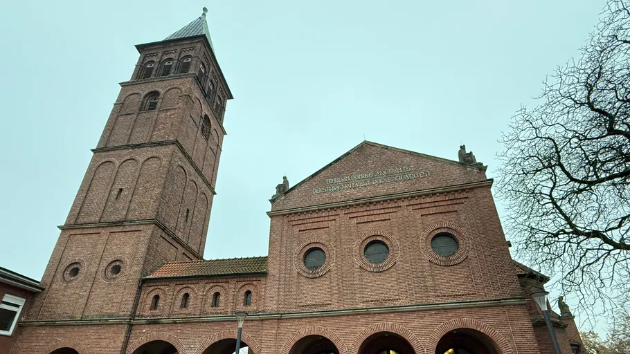 Backsteinkirche mit hohem Turm, bedeckter Himmel.
