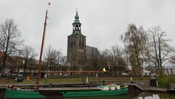 Boat docked near church tower, cloudy day.