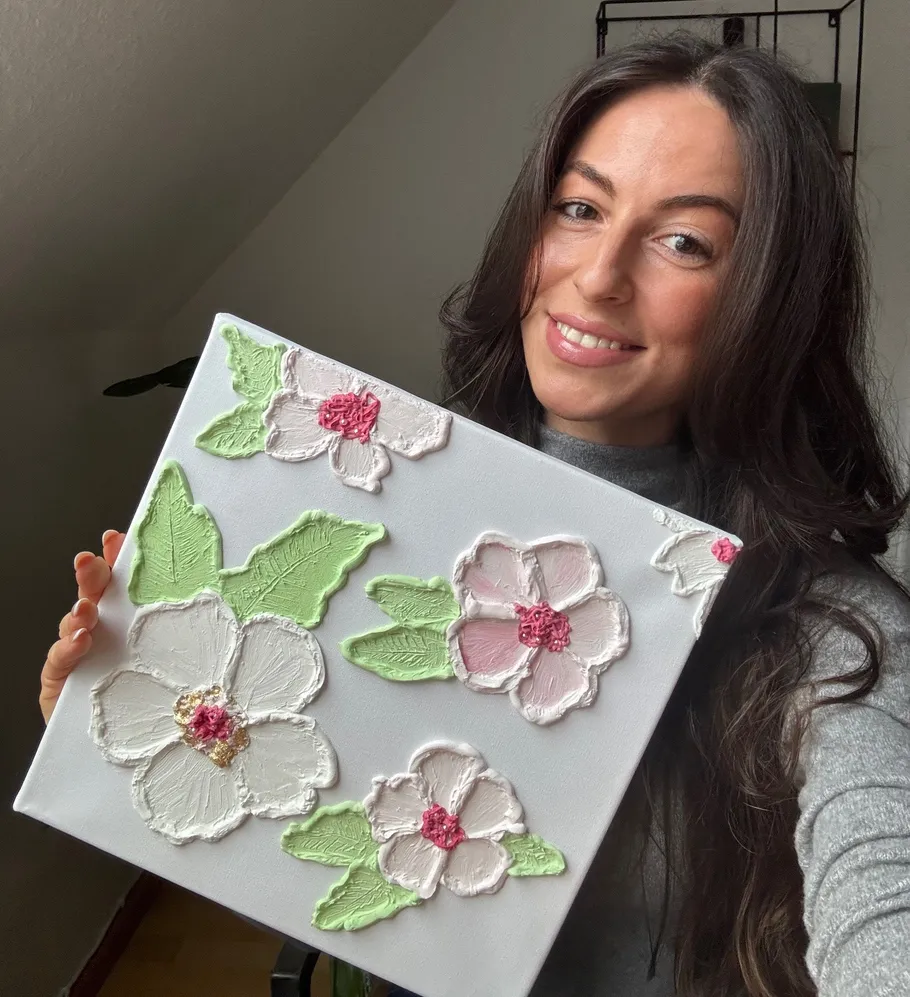 Woman holding floral textured artwork indoors.
