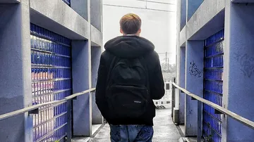 Person geht auf Brücke zwischen blauen Gebäuden.