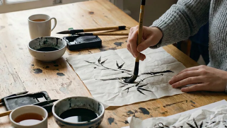 Person painting with brush on paper at table.