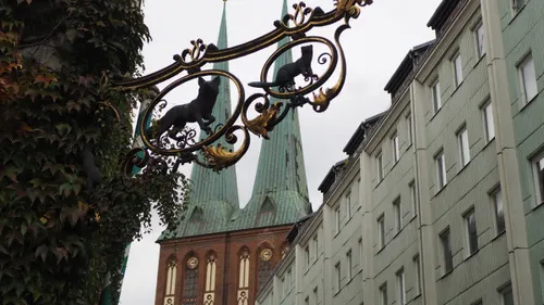 Metallschild mit Katzen, Kirche im Hintergrund.