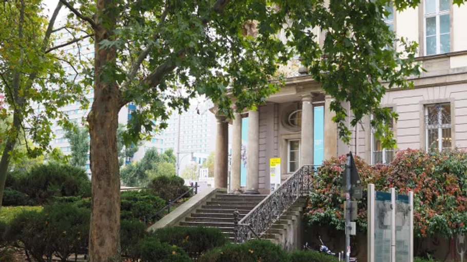 Historisches Gebäude mit Säulen, von Bäumen umgeben.