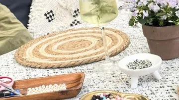 Craft table with beads, drink, plant.