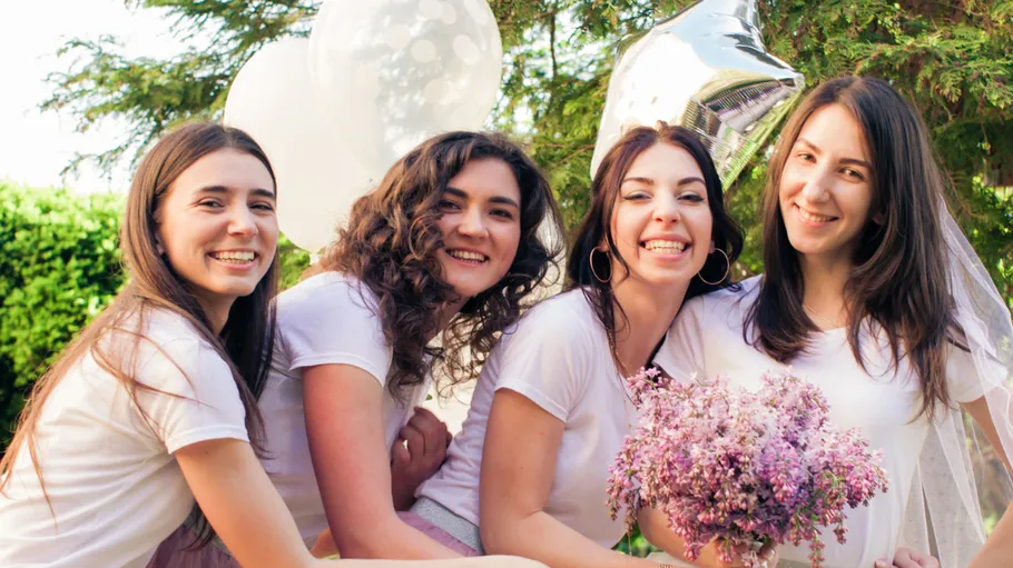 Four women smiling with balloons outdoors.