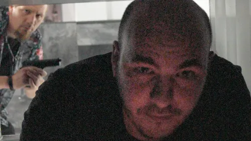 Man with gun sneaks up on another man.