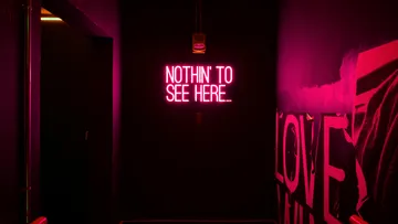 Neonschild an dunkler Wand im Flur.