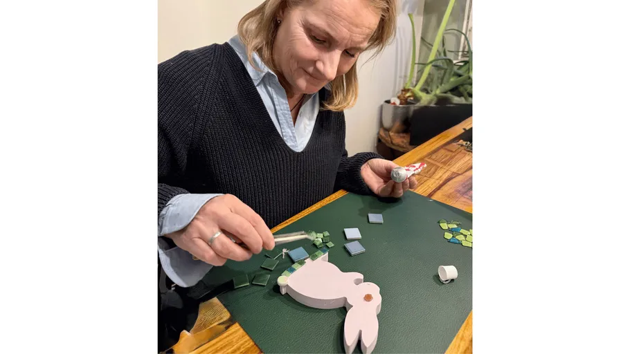 Frau bastelt Mosaik auf Hasenform am Tisch.