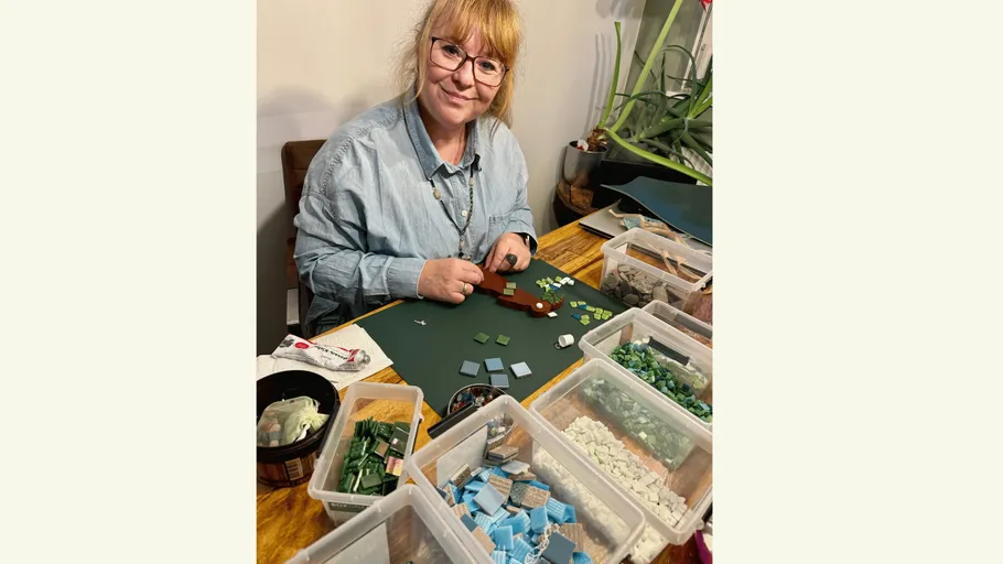 Woman crafting mosaic with tiles at table.