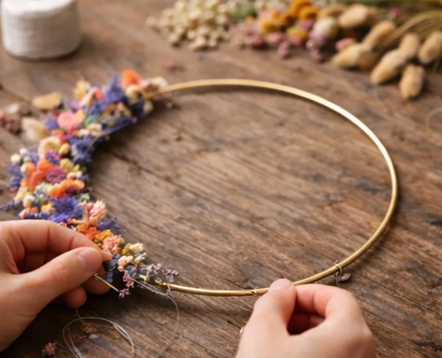 Hands crafting floral wreath on wooden table.