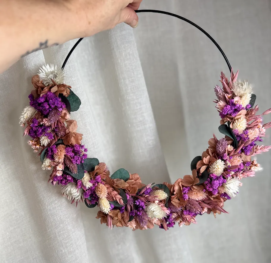 Hand holding floral wreath against curtain.