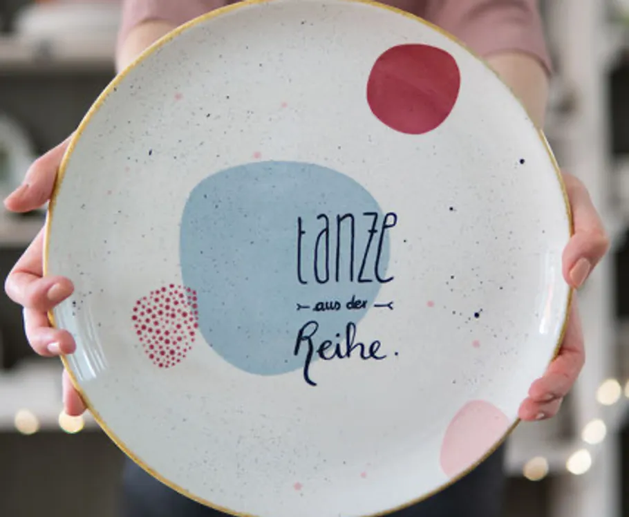Person holds decorated plate with text.