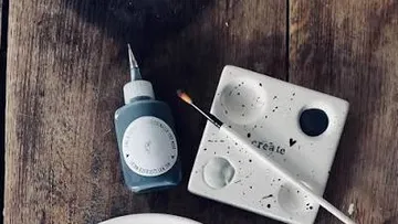 Farbflasche und Pinsel auf Holzoberfläche.