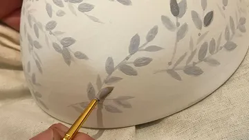 Hand painting leaves on ceramic surface.