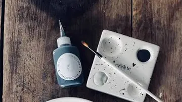Farbflasche und Pinsel auf Holztisch.