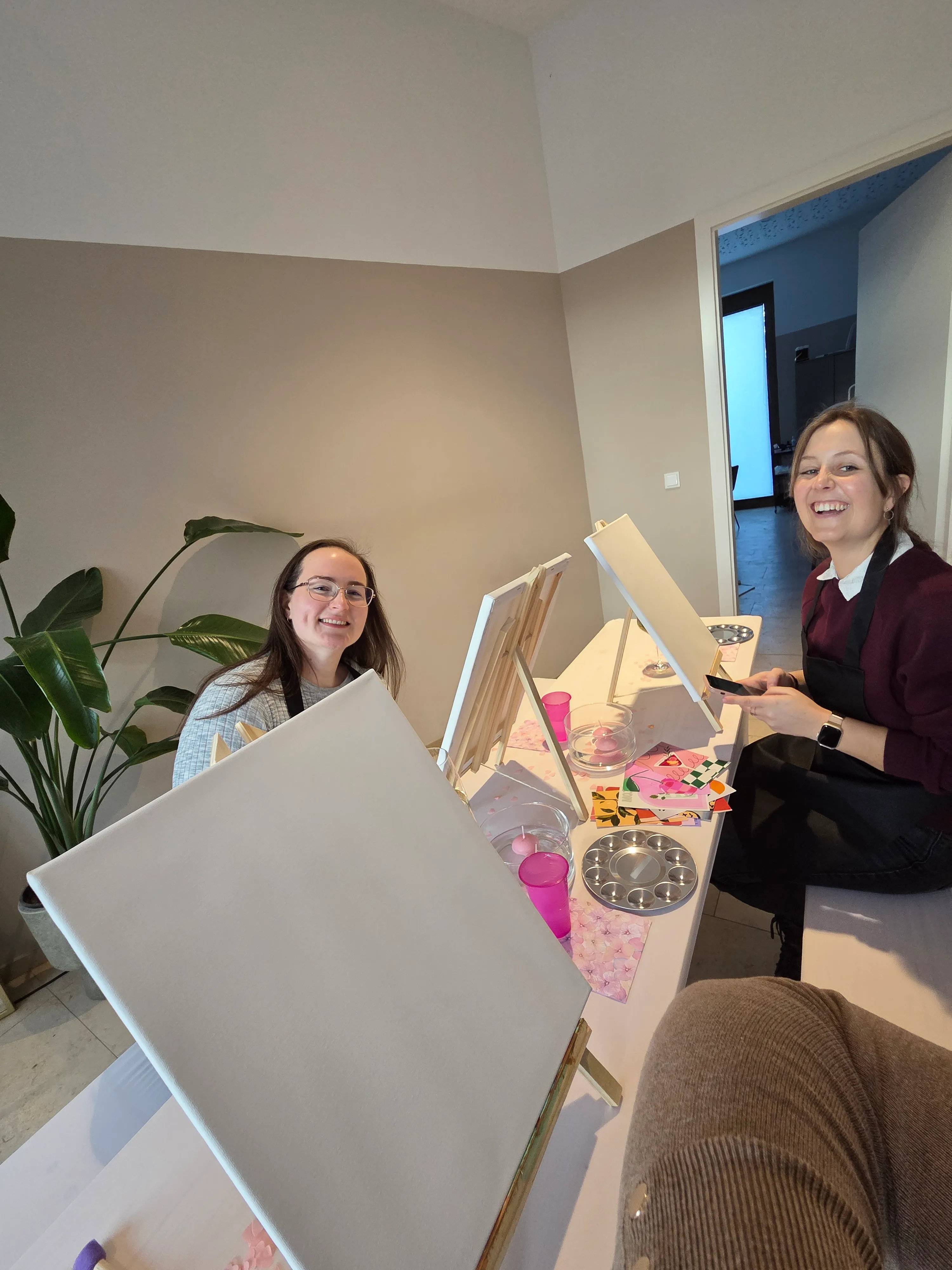 Zwei Frauen lächeln, malen Leinwände drinnen.