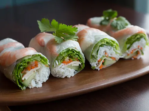 Frische Frühlingsrollen liegen auf einem braunen Holztablett.