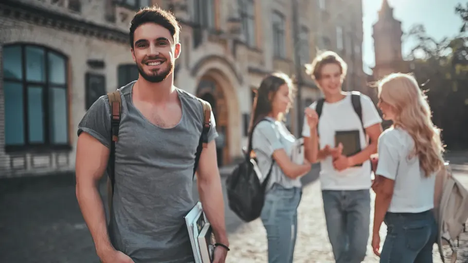 Smiling student holding books, others chatting outside.