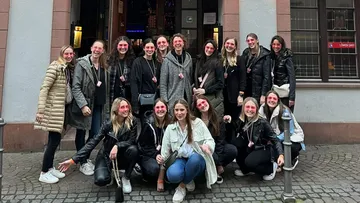 Group of women posing with pink face paint outside.