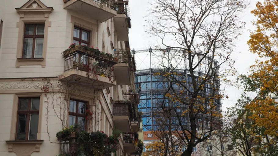 Old building with plants, gasometer nearby.