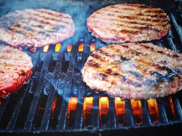 Gegrillte Burger brutzeln über glühenden Kohlen auf Grillrost.