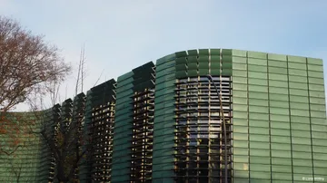 Modern building with green facade and trees.