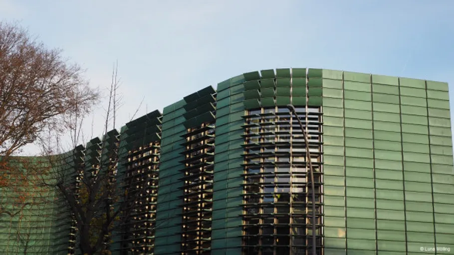 Modern building with green facade and trees.